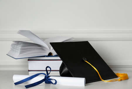 Graduation hat, books and diploma on floor near white wallの写真素材