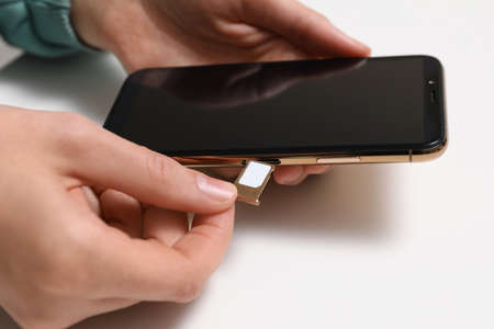 Woman putting SIM card tray in smartphone at white table, closeupの写真素材