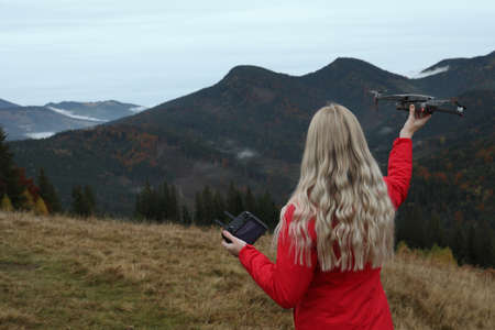 Young woman with modern drone in mountains, back view. Space for text