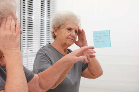 Senior woman looking at reminder note indoors. Age-related memory impairment