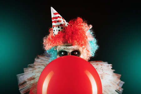 Terrifying clown with red air balloon on black background. Halloween party costumeの写真素材
