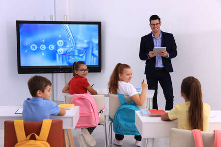 Teacher giving lesson to pupils near interactive board in classroom