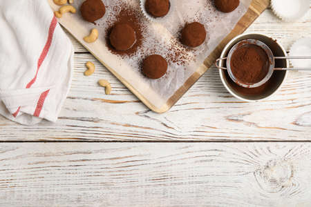 Delicious chocolate truffles with cocoa powder and nuts on white wooden table, flat lay. Space for...