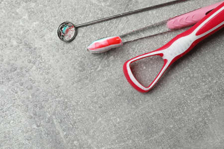 Red tongue cleaner, dentist mirror and toothbrush with paste on gray background. Space for textの写真素材