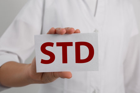 Doctor holding sheet of paper with abbreviation STD on white background, closeupの写真素材