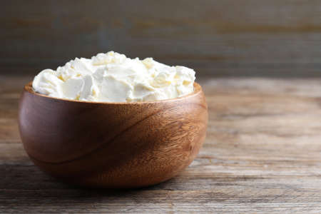 Bowl of tasty cream cheese on wooden table, space for textの写真素材