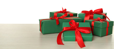 Green gift boxes with red bows on wooden table against white background, space for text