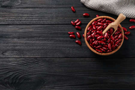 Raw red kidney beans with bowl, scoop and napkin on dark wooden table, flat lay. Space for textの写真素材