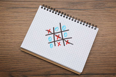 Notebook with tic tac toe game on wooden table, top view