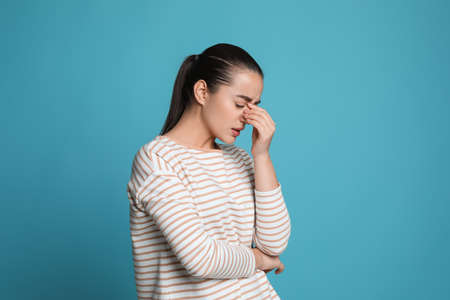 Young woman suffering from headache on light blue background