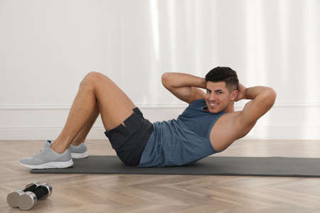 Handsome man doing abs exercise on yoga mat indoors