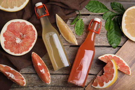Glass bottles of different pomelo juices and fruits on wooden table, flat layの写真素材