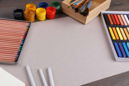 Blank sheet of paper, colorful chalk pastels and other drawing tools on wooden table. Modern...