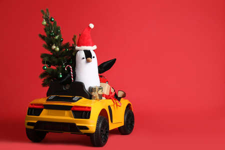 Child's electric car with toys, gift boxes and Christmas tree on red background, space for textの写真素材