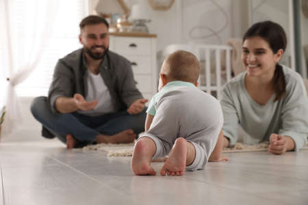 Happy parents watching their baby crawl on floor at homeの写真素材