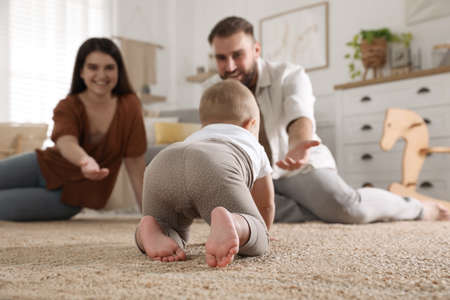 Happy parents watching their baby crawl on floor at homeの写真素材