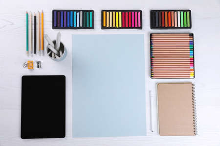 Layout with blank paper, soft pastels and other drawing supplies on white wooden table at artist's...