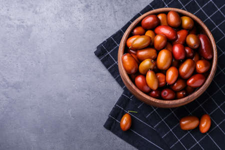 Wooden bowl of ripe red dates and napkin on gray table, top view. Space for text