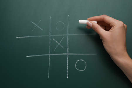 Woman playing tic tac toe game on green chalkboard, top viewの写真素材