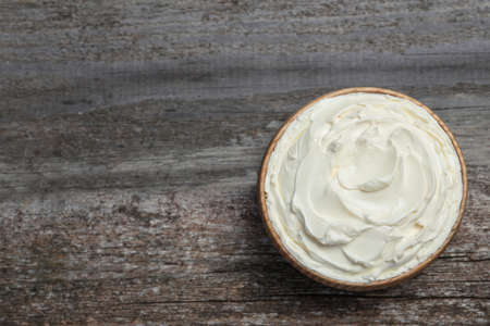 Bowl of tasty cream cheese on wooden table, top view. Space for textの写真素材