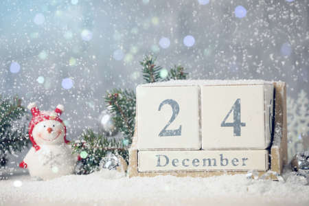 December 24 - Christmas Eve. Snow falling onto wooden block calendar and festive decor against...
