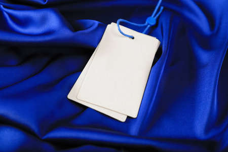 Blank white tags on blue silky fabric, closeup. Space for textの写真素材