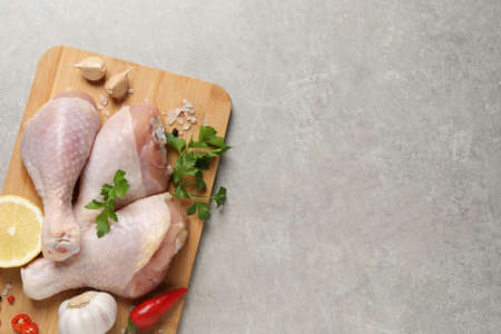 Wooden board with fresh raw chicken legs and other products on light gray table, top view. Space for textの写真素材