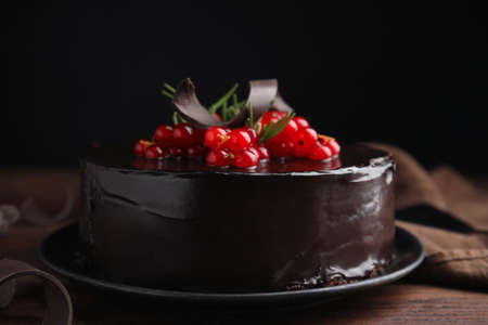Tasty homemade chocolate cake with berries and rosemary on wooden table against black background,...