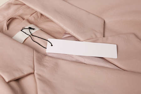 Blank white tag on beige leather jacket, closeup. Space for text