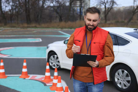 Instructor with clipboard near car on test track. Driving schoolの写真素材