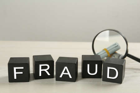 Black cubes with word Fraud, magnifying glass and money on white table, space for textの写真素材