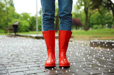 Woman wearing red rubber boots outdoors after thunderstorm with hail, closeup