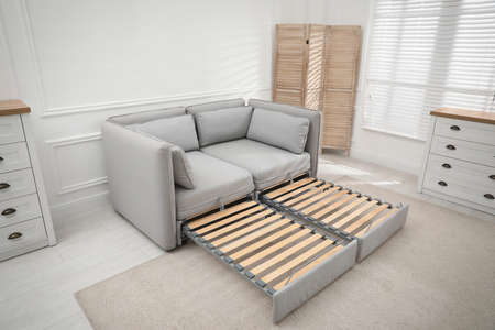 Stylish room interior with sleeper sofa near white wall. Additional place for guest