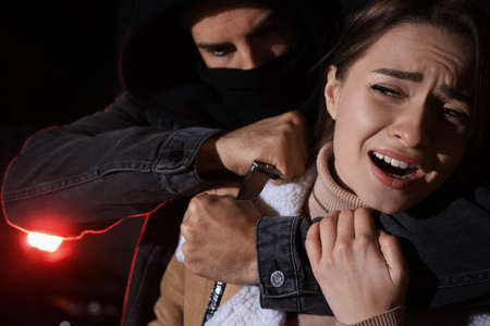 Criminal with knife attacking young woman outdoors at night. Self defense conceptの写真素材
