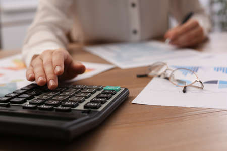 Tax accountant with calculator working at wooden table, closeup