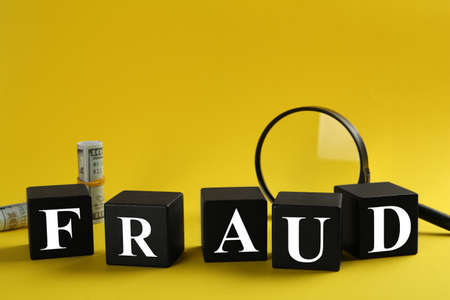 Black cubes with word Fraud, magnifying glass and money on yellow background, space for textの写真素材