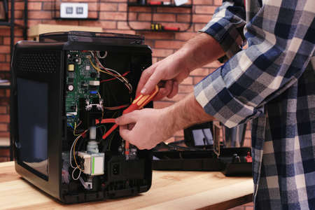 Man with screwdriver fixing coffee machine at table indoors, closeup
