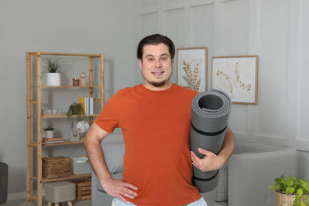 Overweight man with yoga mat at homeの写真素材