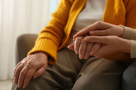 Young and elderly women holding hands together indoors, closeup. Space for textの写真素材
