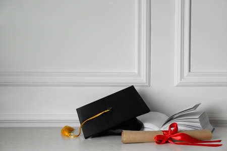 Graduation hat, book and diploma on floor near white wall, space for textの写真素材