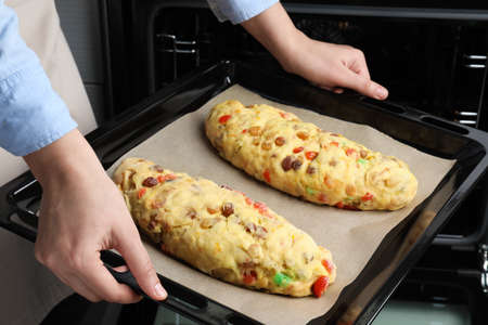 Woman putting baking tray with raw homemade Stollens into oven, closeup. Traditional German...