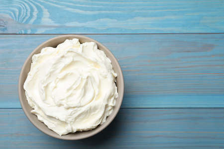 Bowl of tasty cream cheese on light blue wooden table, top view. Space for textの写真素材