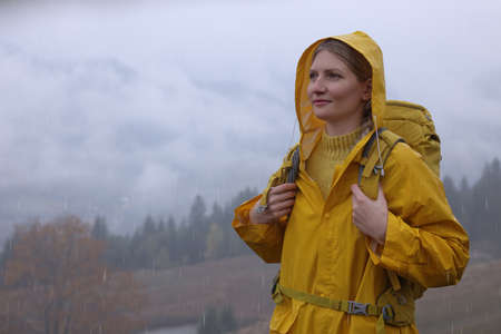 Young woman in raincoat enjoying mountain landscape under rainの写真素材