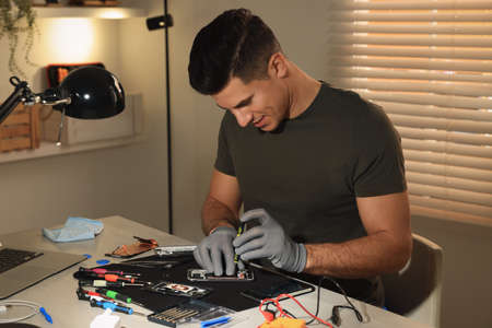 Technician repairing broken smartphone at table indoors