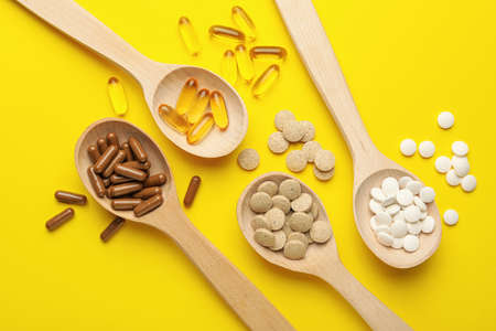Wooden spoons and different dietary supplements on yellow background, flat layの写真素材