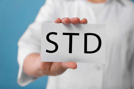 Doctor holding sheet of paper with abbreviation STD on light blue background, closeupの写真素材