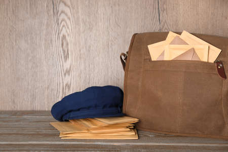 Postman's hat near bag full of letters on wooden background. Space for text