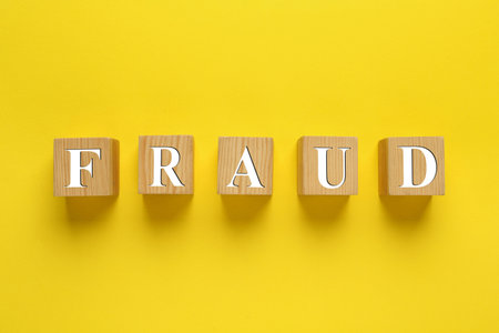 Wooden cubes with word Fraud on yellow background, flat layの写真素材