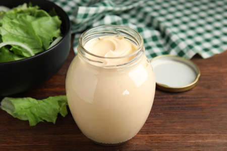 Jar of delicious mayonnaise and fresh salad on wooden tableの写真素材