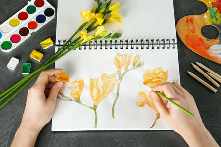 Woman drawing beautiful freesia flowers in sketchbook at black table, above viewの写真素材